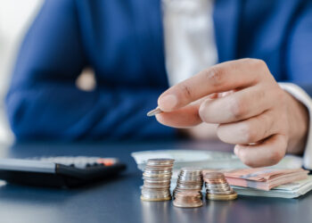 Businessman,Holding,Euro,Cents,Coins,Dollar,Bills,On,Table,With